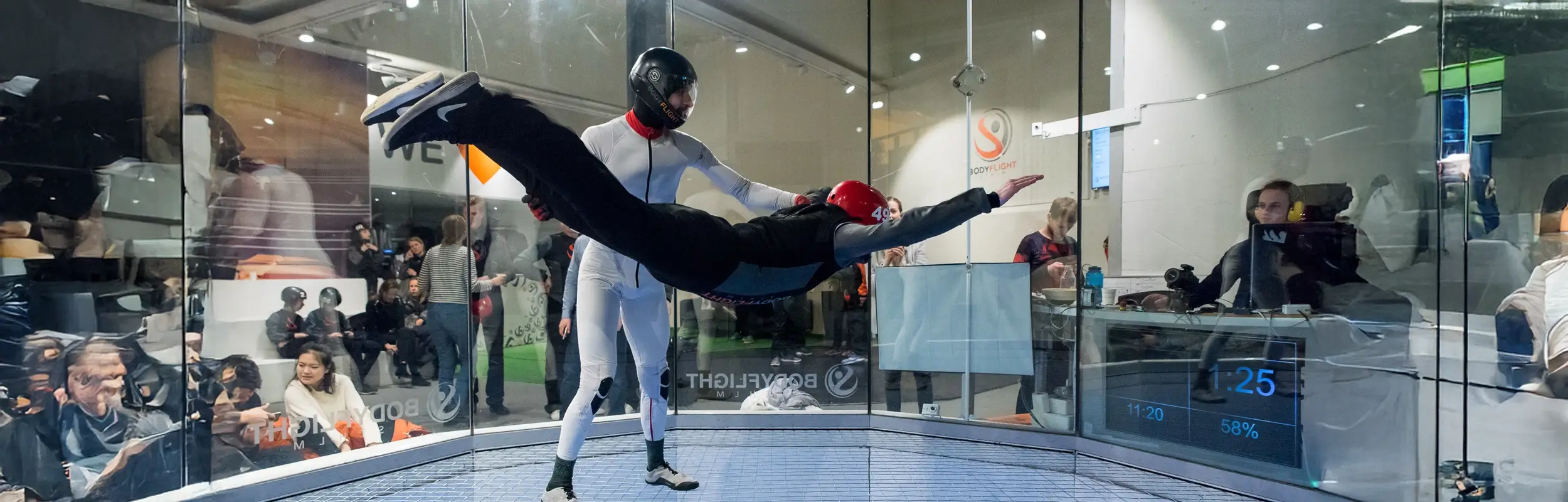 Person med röd hjälm som flyger i vindtunnel. Testa på hur det känns att flyga i ett rör hos oss.